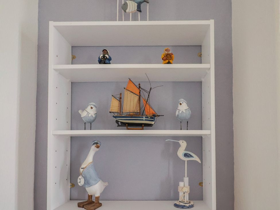 A shelf with decorative items including a boat and bird figurines at Flat F Bay House in West Bay