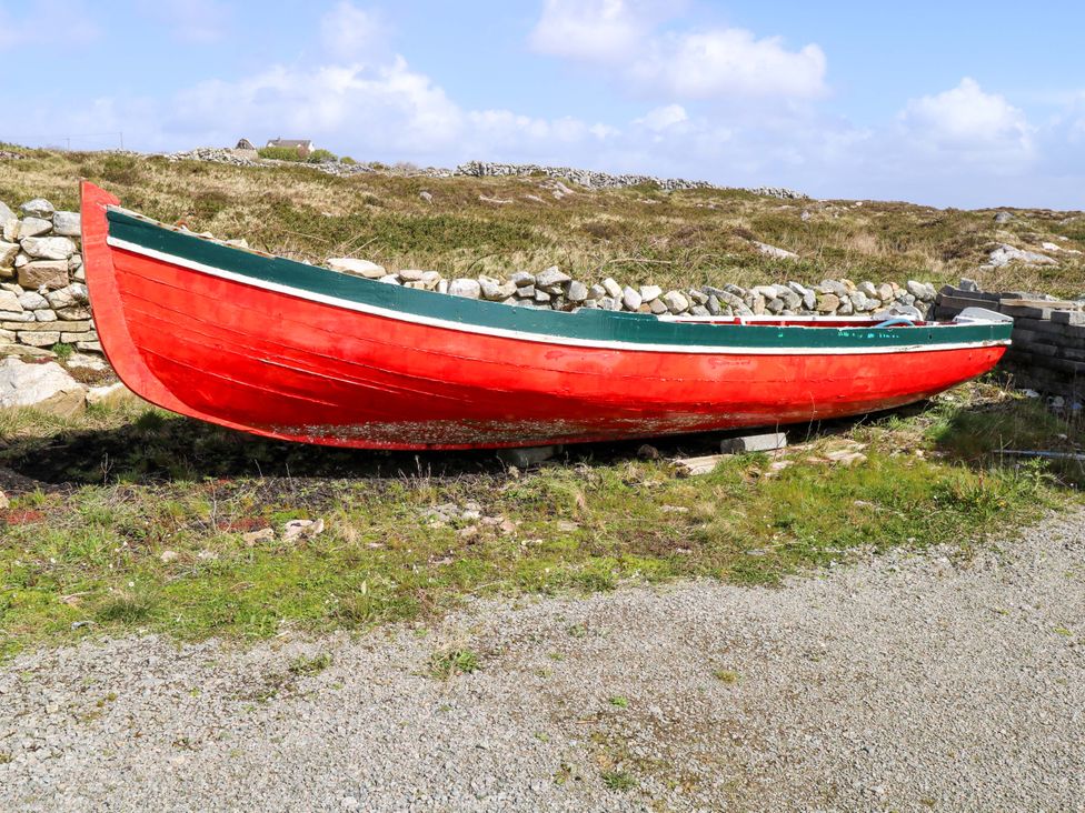 A red boat on land surrounded by grass and stone wall at Tí Tom Nárta, Trabane near Lettermore, County Galway