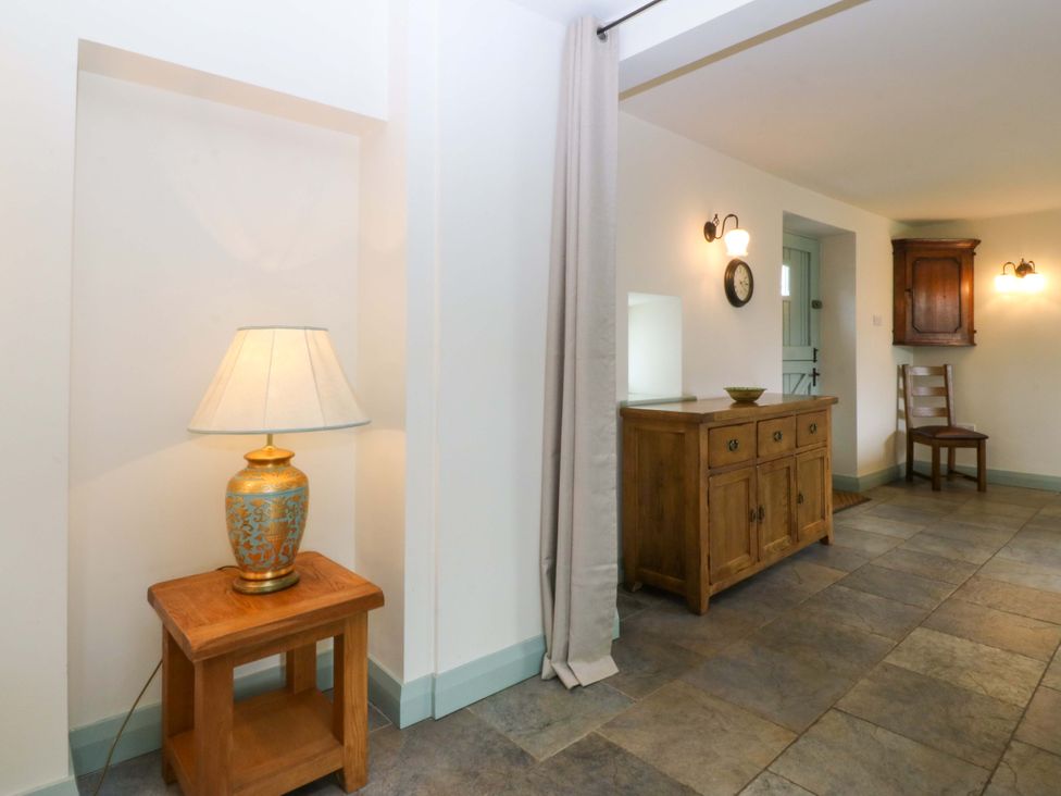 A hallway with a lamp, clock, table and chair at No 2 The Stables Capel Coch near Llannerch-Y-Medd