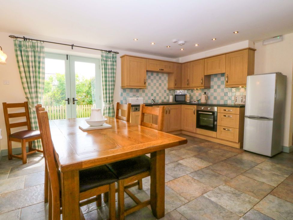 A kitchen with wooden dining table and cabinets at No 2 The Stables Capel Coch near Llannerch-Y-Medd