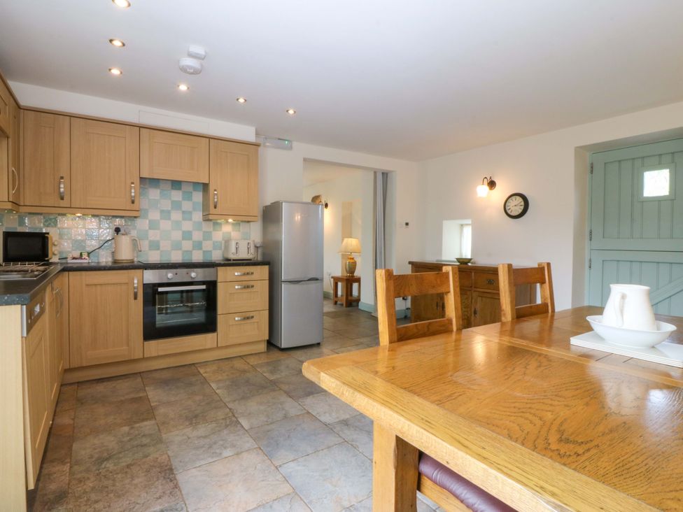 A kitchen with wooden cabinets and a dining table at No 2 The Stables Capel Coch near Llannerch-Y-Medd