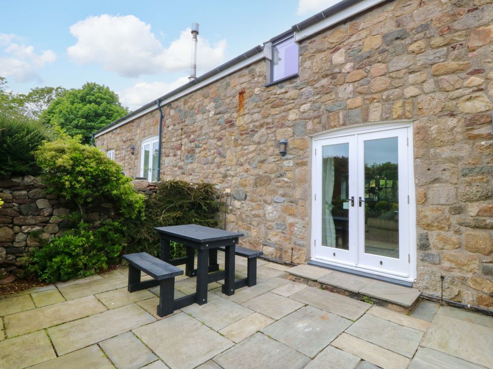 An outdoor area with a stone wall, table, and benches at No 2 The Stables Capel Coch near Llannerch-Y-Medd