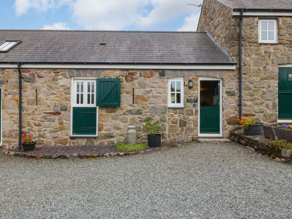 A stone cottage exterior with green doors and gravel entrance at No 3 The Dairy Capel Coch near Llannerch-Y-Medd