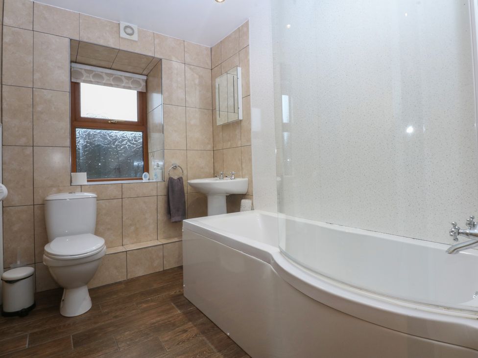 A bathroom with a bathtub, sink, toilet and window at Llofft Yr Yd Porthmadog