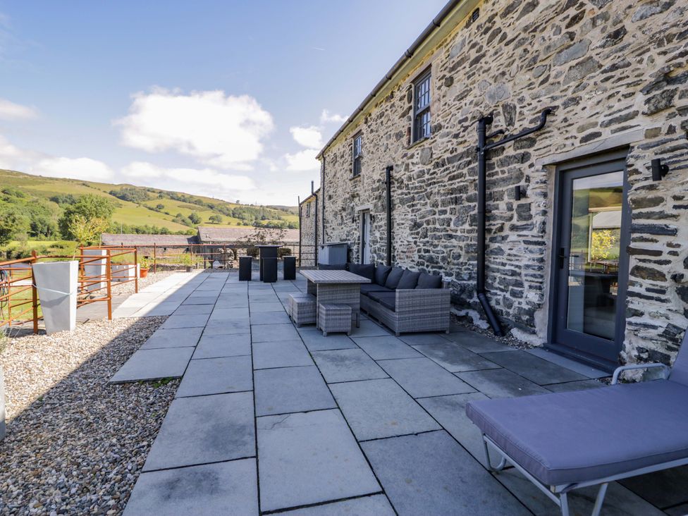 An outdoor seating area with stone wall and patio at Plas Glan Yr Afon in Llangernyw