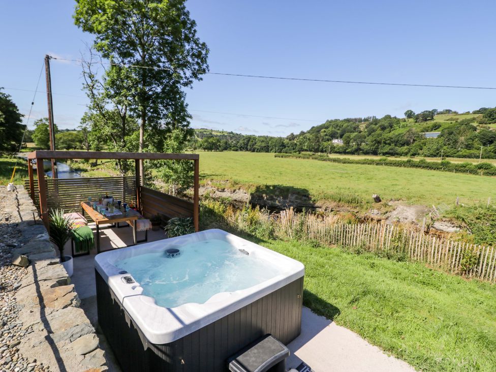 An outdoor area with a hot tub and seating at Plas Glan Yr Afon in Llangernyw