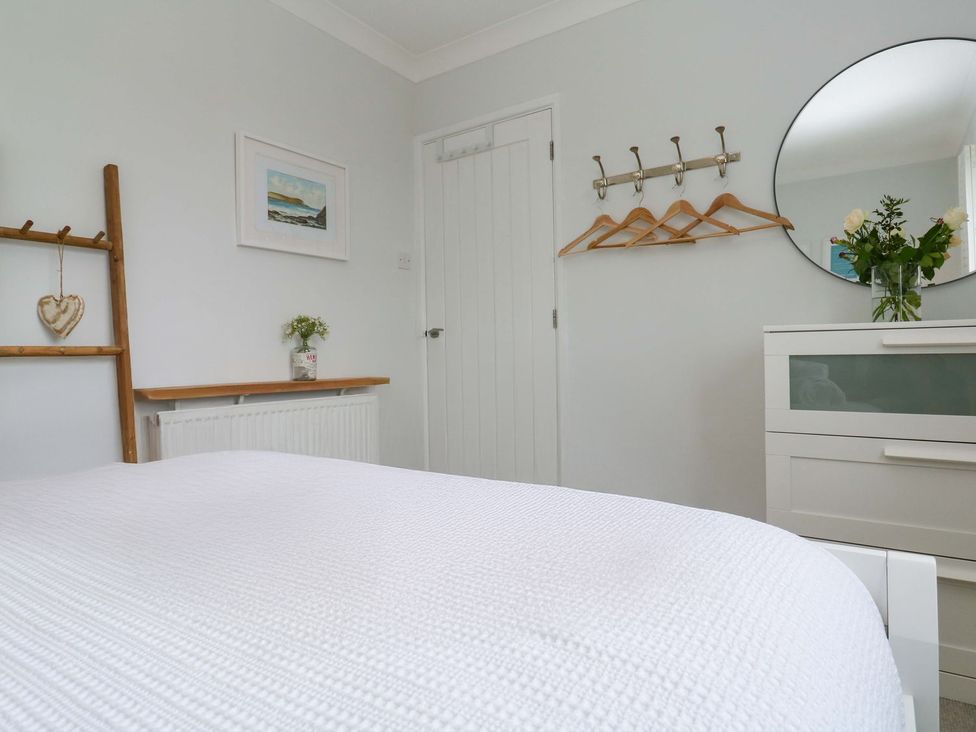 A bedroom with a bed, mirror, and coat hooks at Trelowen St Issey near Padstow