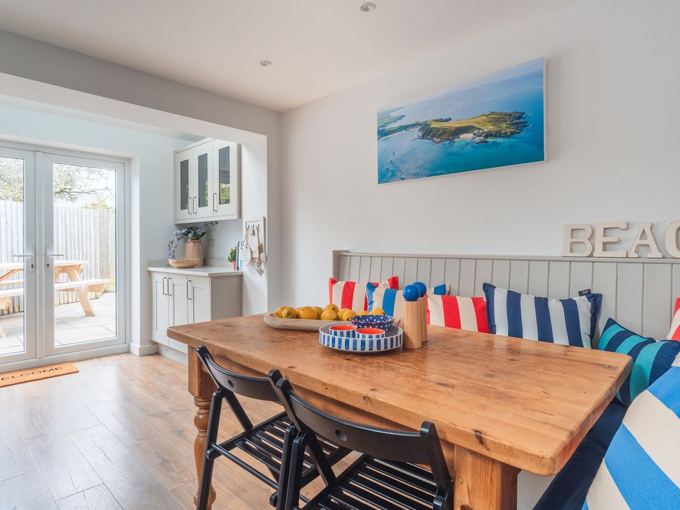 A dining room with a wooden table and striped cushions at Gerallt in Morfa Nefyn