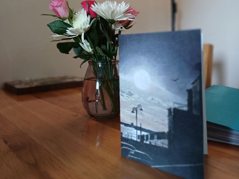 A vase with flowers and a card on a table at Barton Cottage in Bridport