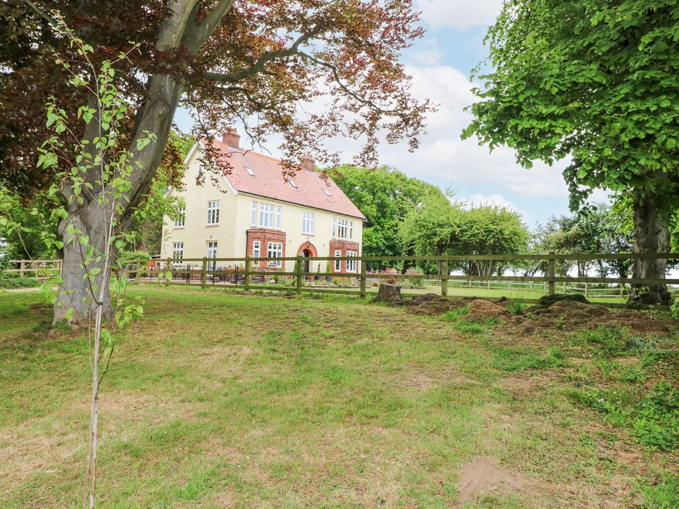 A two-story house with a red roof surrounded by trees and a wooden fence at High House in Southrepps