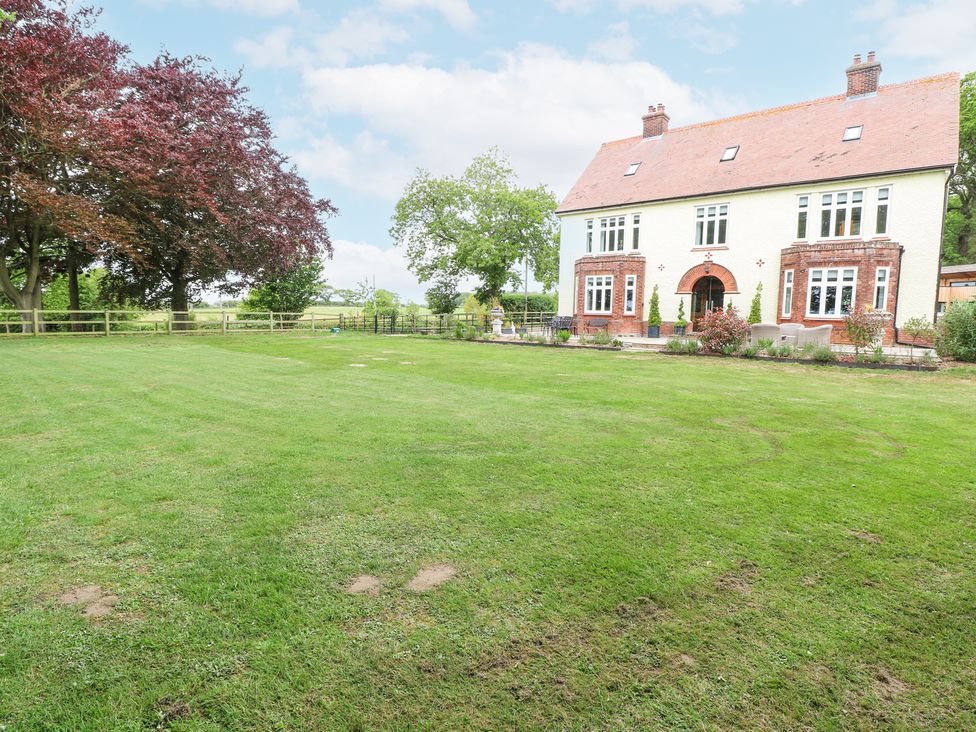 A large lawn with trees and a two-story house with a tiled roof at High House in Southrepps