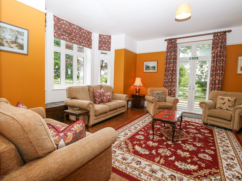 A living room with sofas tables a lamp and patterned curtains at High House in Southrepps