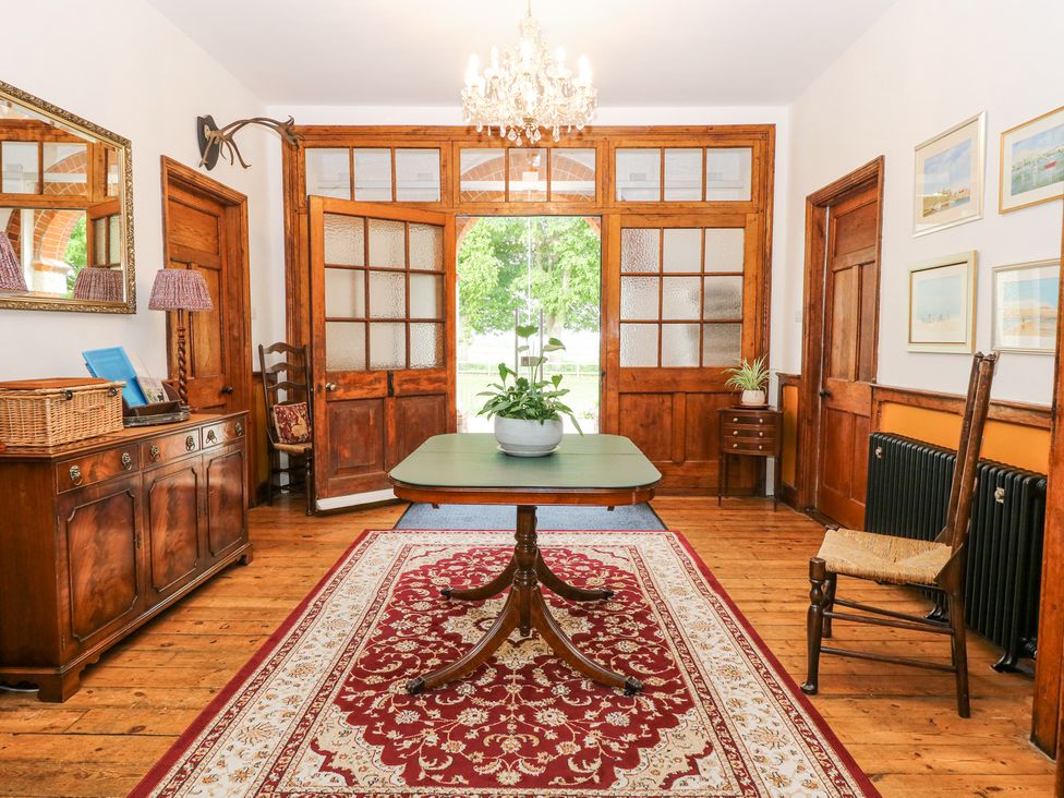 A room with wooden doors and floor a table with a plant in the center and a red patterned rug at High House in Southrepps