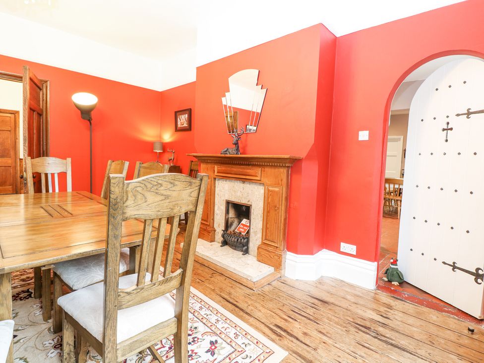 A dining room with wooden table and chairs a fireplace and red walls at High House in Southrepps