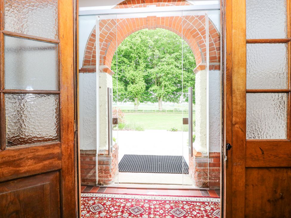 An entrance with wooden doors opening to a glass door and a brick archway overlooking a lawn and trees at High House in Southrepps