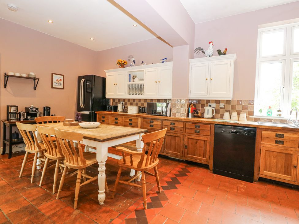 A kitchen with a wooden dining table and chairs wooden cabinets and a black refrigerator at High House in Southrepps