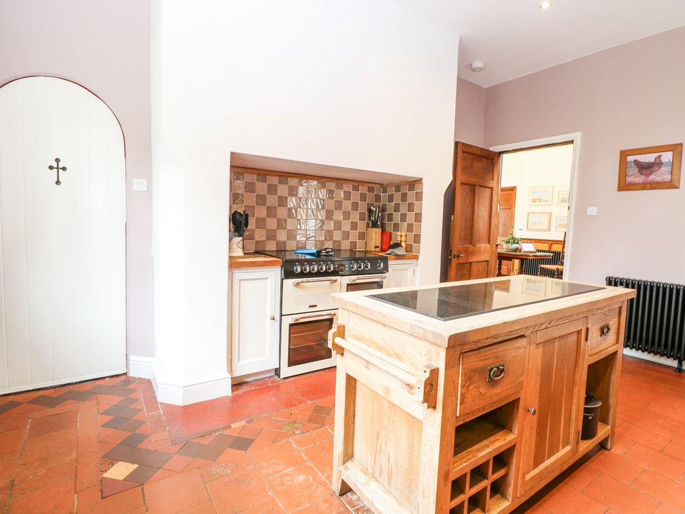 A kitchen with a wooden island and stove with tiled backsplash at High House in Southrepps