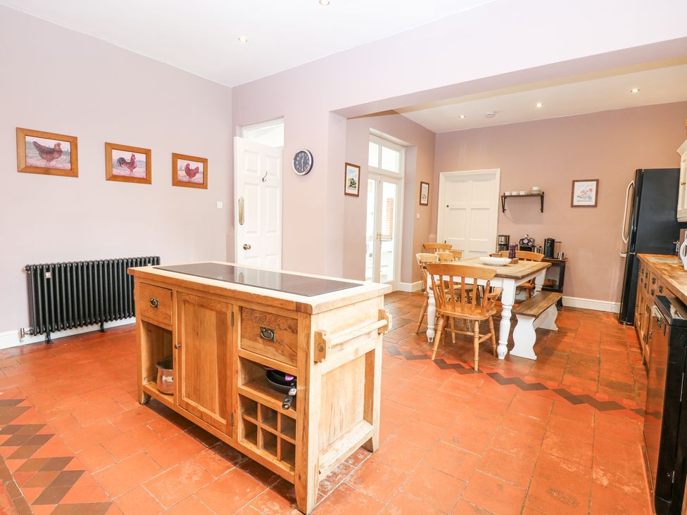 A kitchen with a wooden island in the center a dining table with chairs and bench and framed pictures on the walls at High House in Southrepps