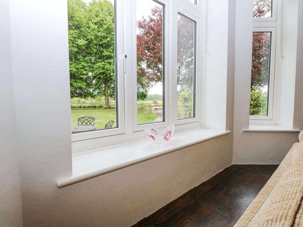 A seating area with a beige sofa near corner windows overlooking a garden at High House in Southrepps