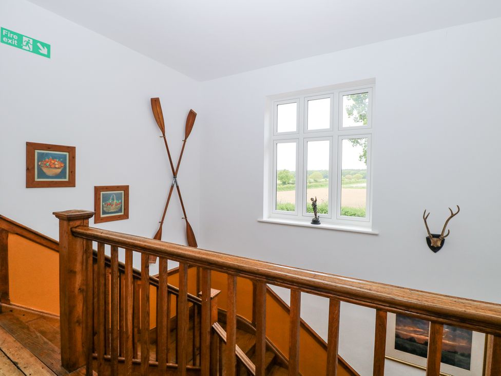 A staircase with wooden railing and walls decorated with crossed oars paintings and a mounted antler at High House in Southrepps