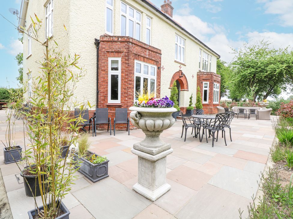 An outdoor patio with tables chairs potted plants and a large flower urn at High House Southrepps