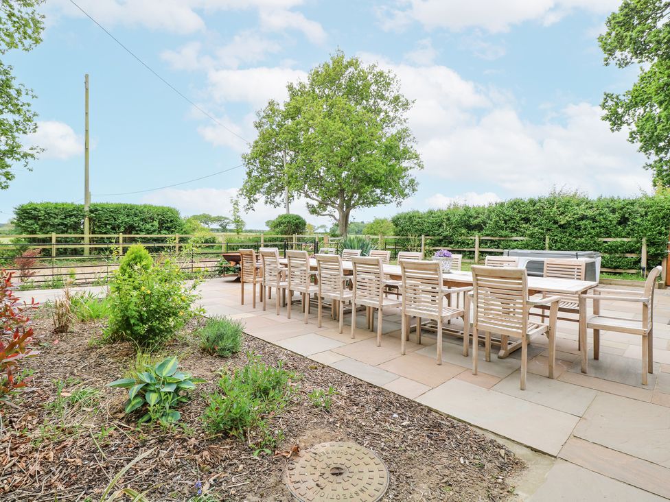 An outdoor patio with a long wooden dining table and chairs surrounded by plants and trees at High House in Southrepps
