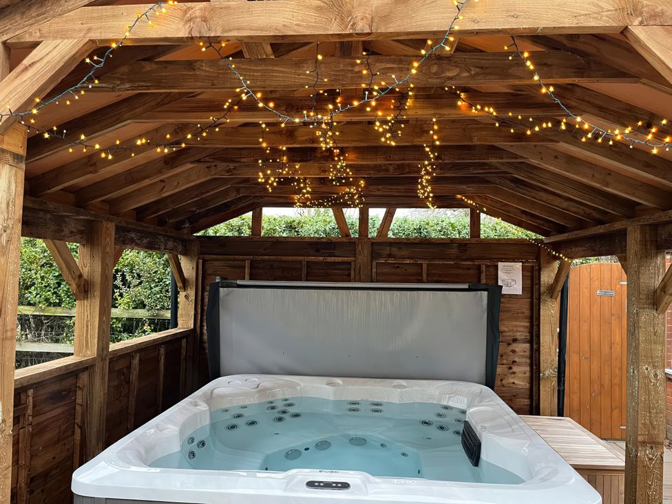 An outdoor area with a hot tub under a wooden structure at High House in Southrepps