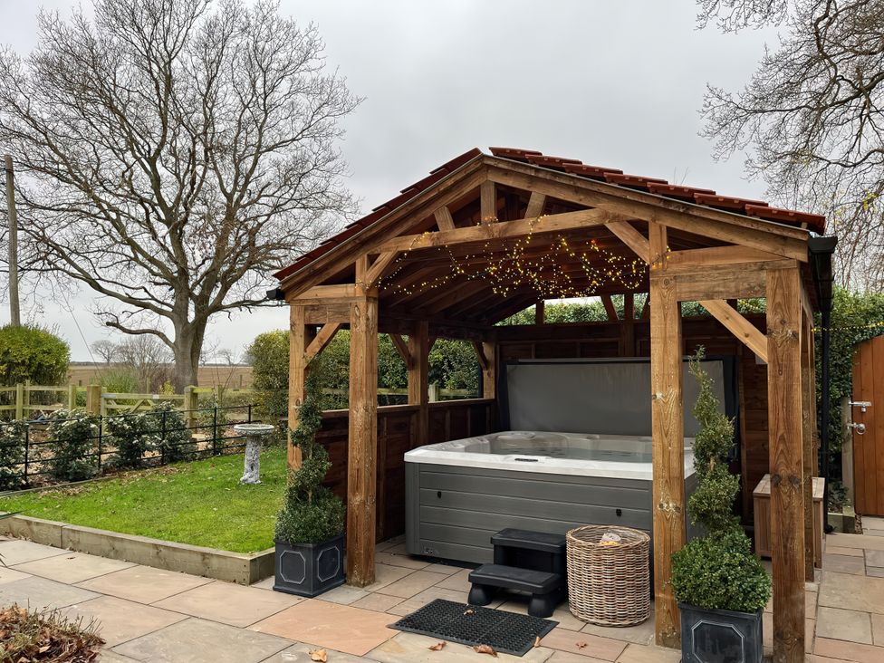 A garden with a hot tub under a wooden gazebo at High House in Southrepps