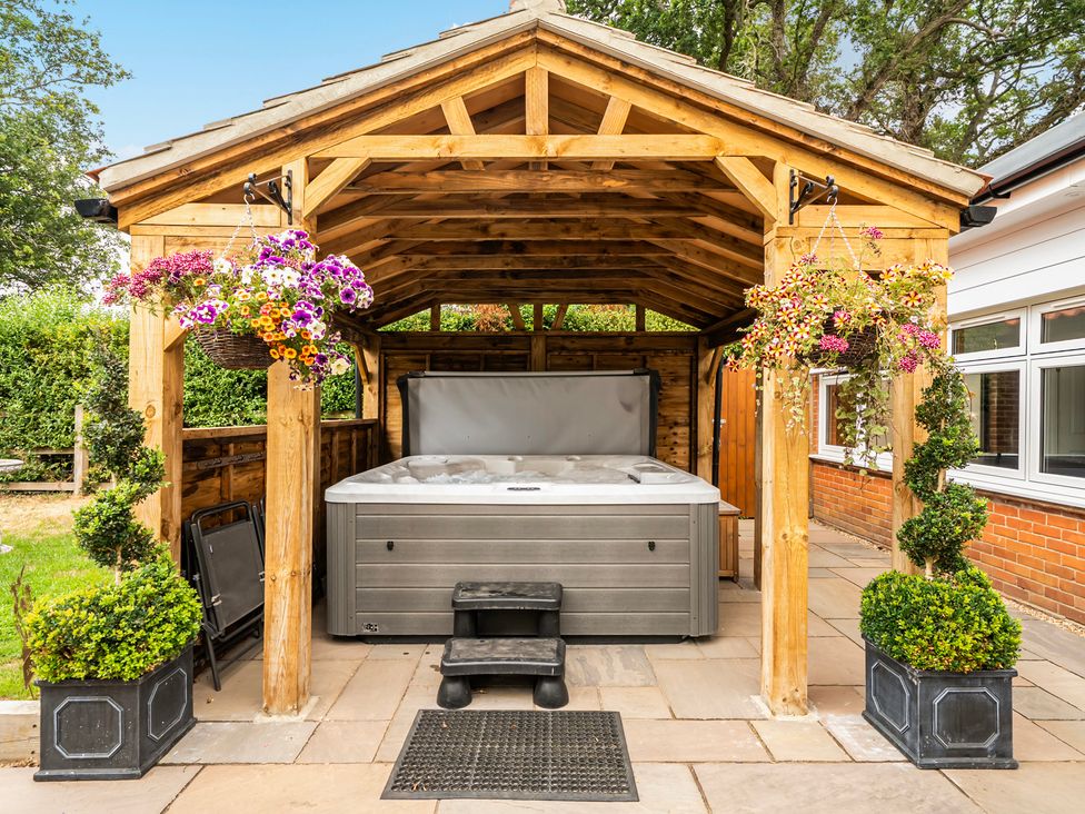 A hot tub under a roof with flowers and planters at High House Southrepps