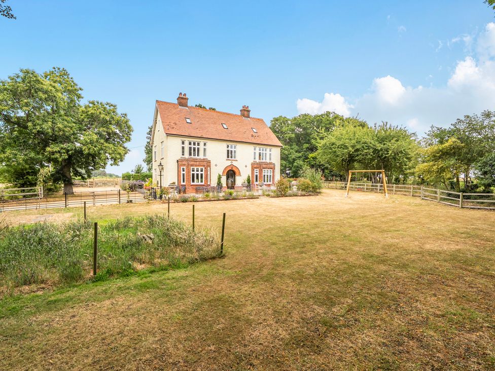 A house with a swing set and trees in the garden at High House in Southrepps
