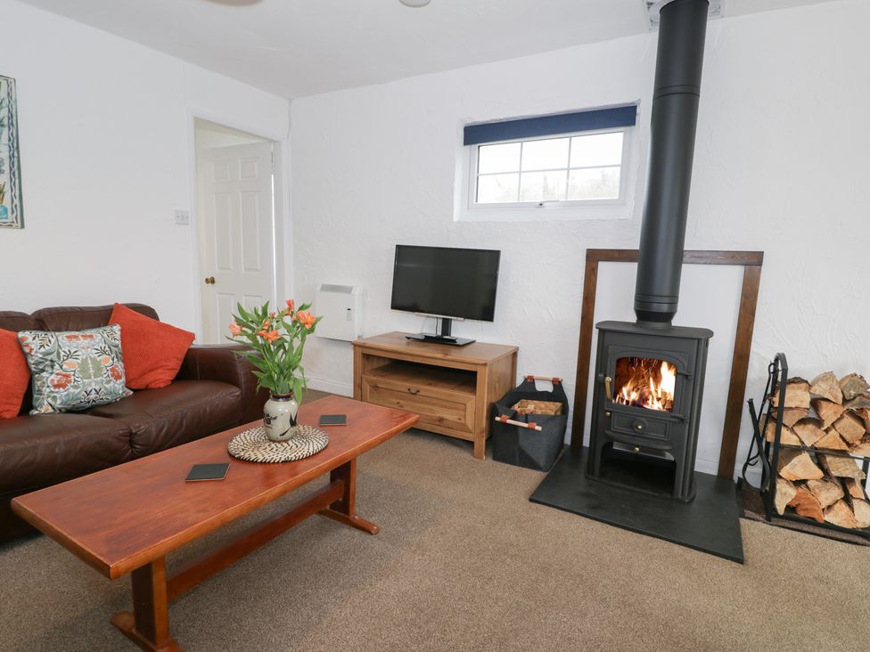 A living room with a sofa, TV, and wood stove at Min Y Mor Llanystumdwy near Criccieth