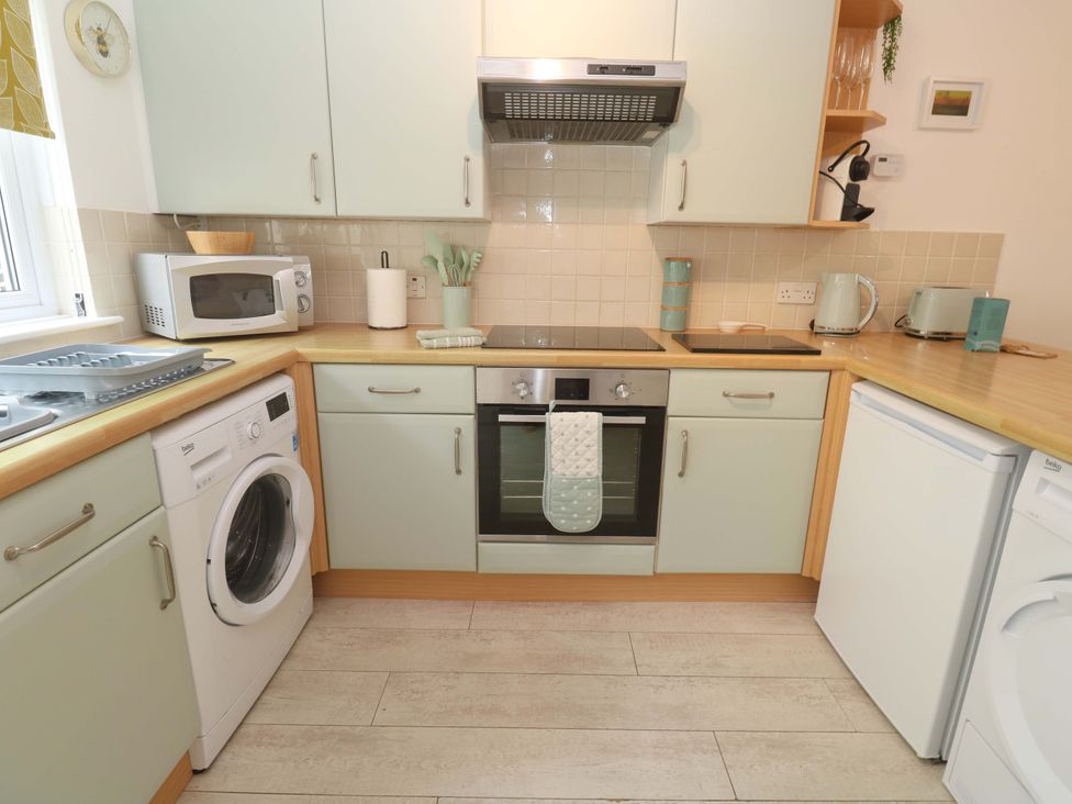 A kitchen with appliances including washing machine and microwave at Driftwood in Marazion