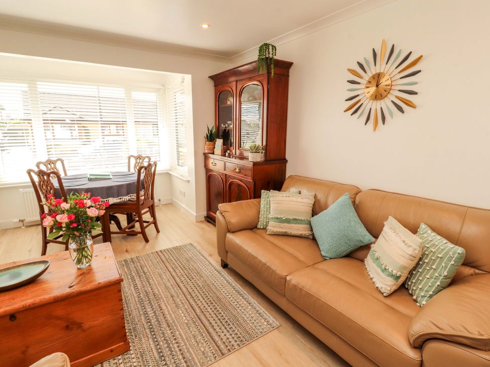 A living room with a sofa, dining table, and clock at The Paddock in Kirkcowan