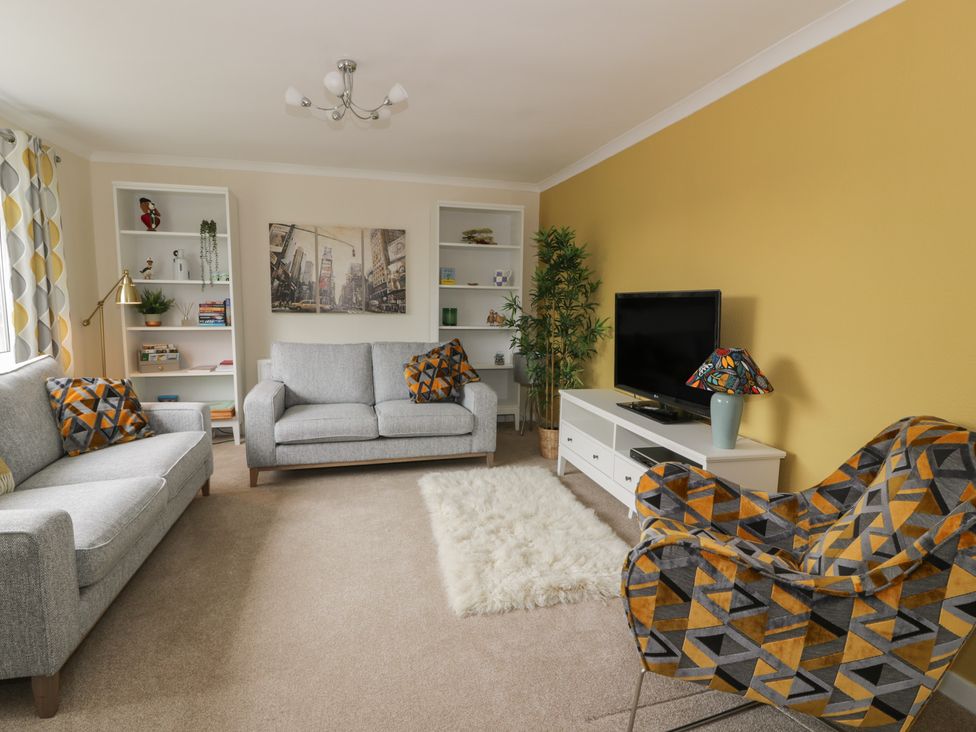 A living room with a sofa, armchair, and television at The Rowans 