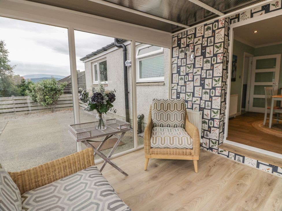 A conservatory with an armchair and a table at The Rowans in 