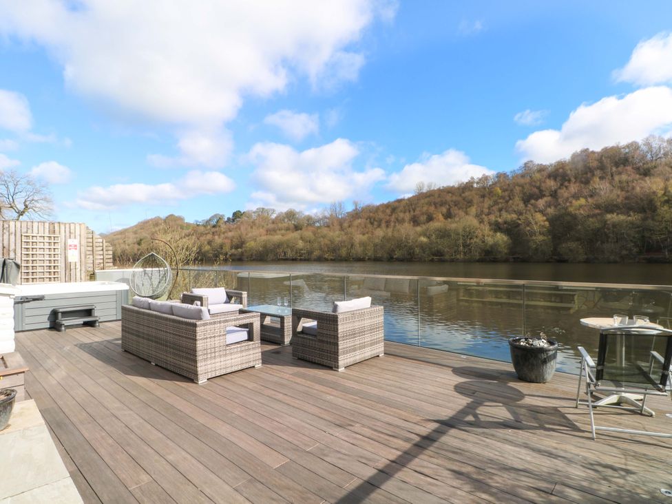 A deck with outdoor furniture and a hot tub by a river at The Bothy in Leek