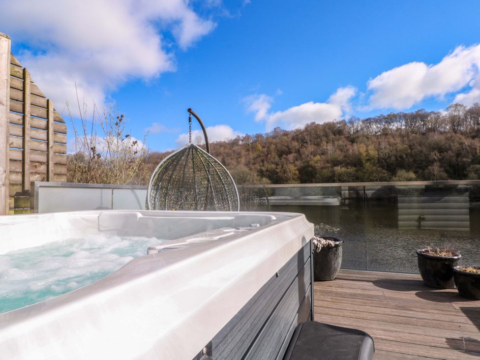 A hot tub on a deck with a hanging chair overlooking the water at The Bothy in Leek