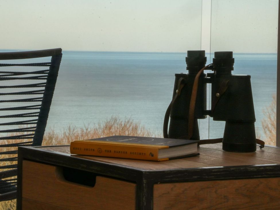 A table with binoculars and a book beside a chair and a view of the sea at The Lookout