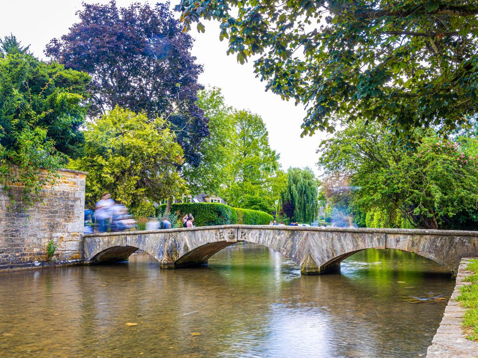 A bridge over a river with trees and people at Mallards in Bourton-On-The-Water