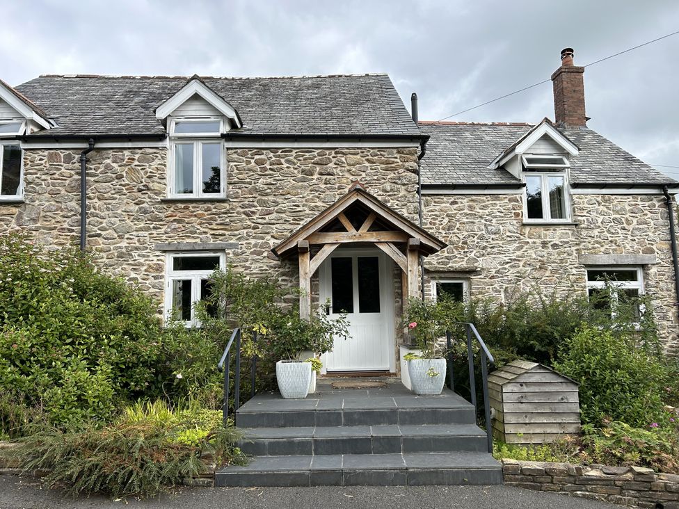 A stone house with a wooden front door and steps at Middle Dean Farmhouse Trentishoe near Parracombe