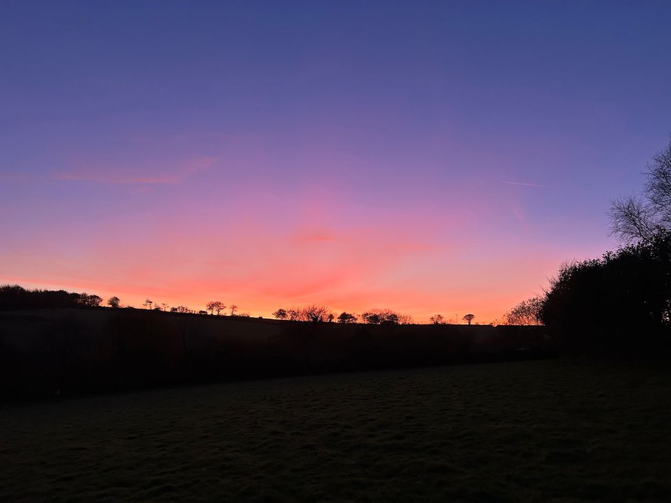A sunset over a field with trees at Middle Dean Farmhouse near Parracombe