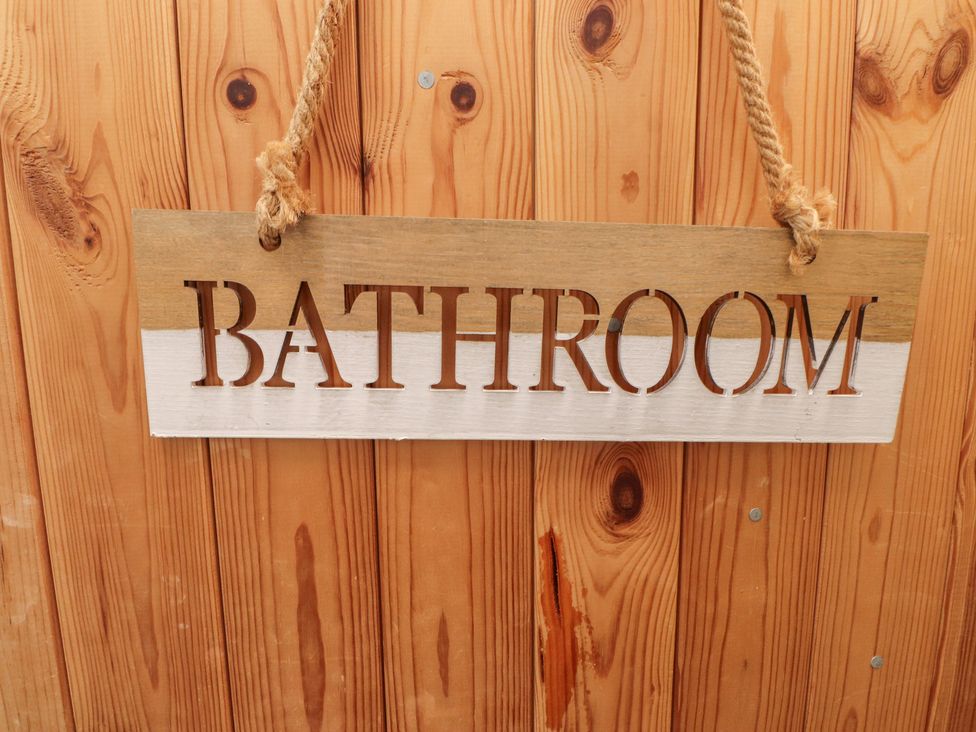 A bathroom sign made of wood hanging on a wall at Menuchah in Criccieth