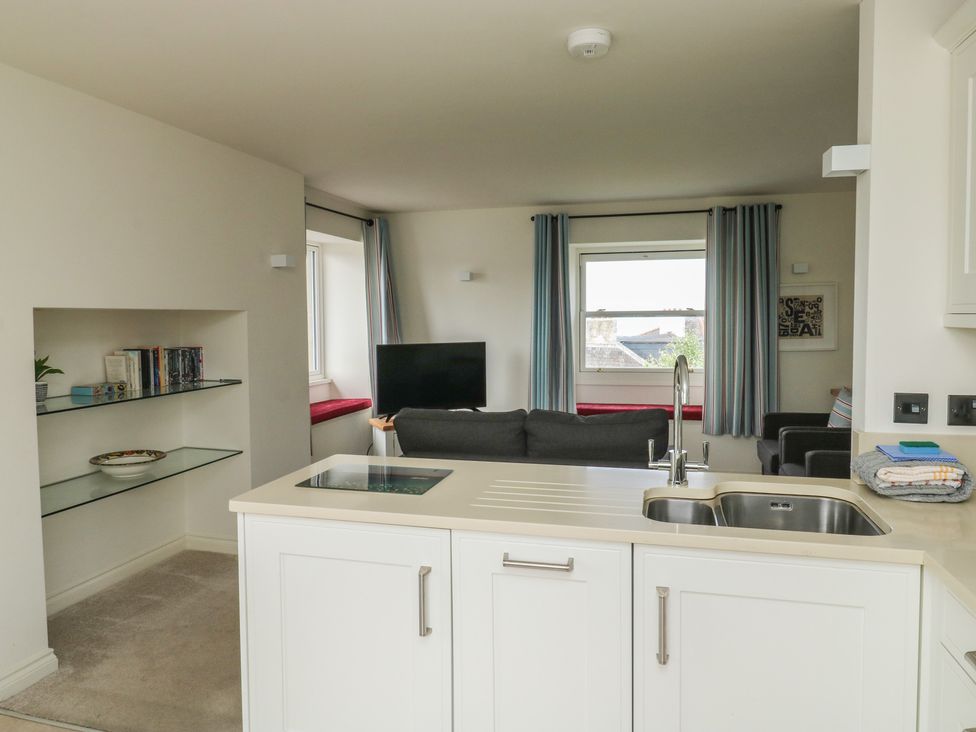 A kitchen with a sink and a living area with a sofa and television at Bay View in Brixham