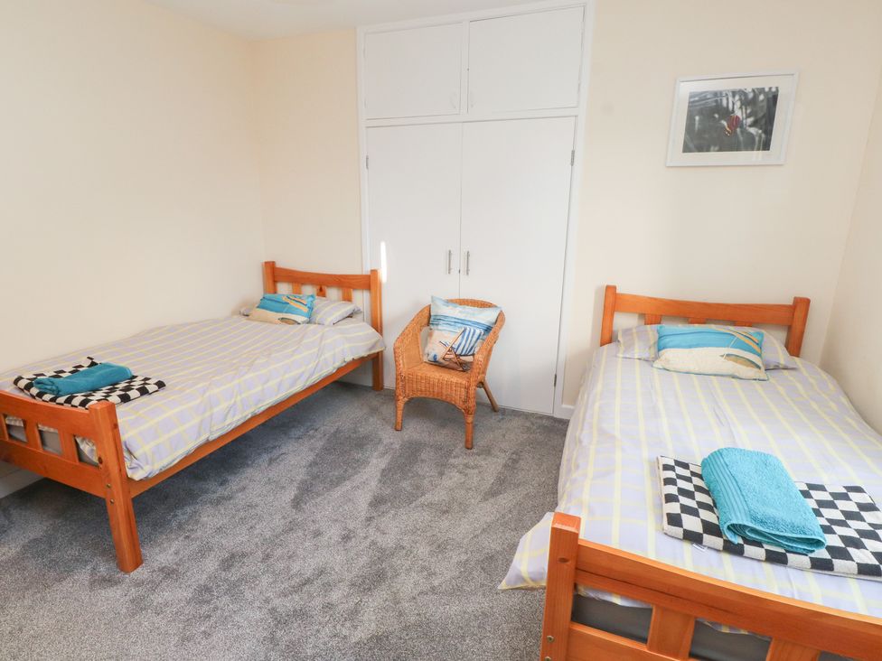 A bedroom with two beds and a wicker chair at Glan Aber in Pwllheli