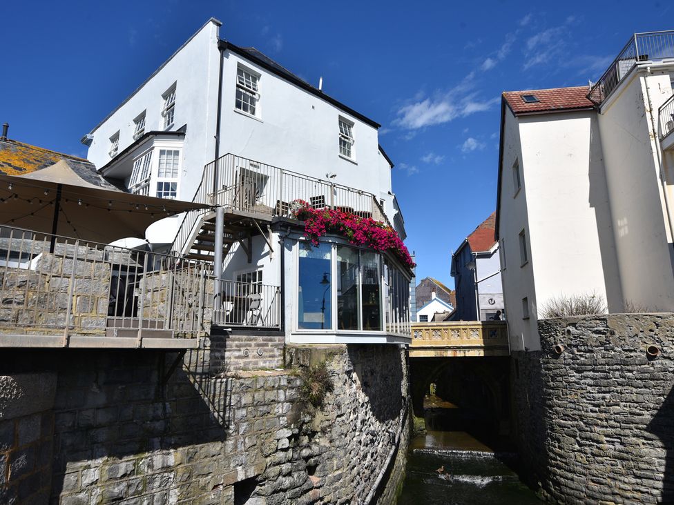 A building with a balcony and flowers over a waterway at The Nest in Lyme Regis
