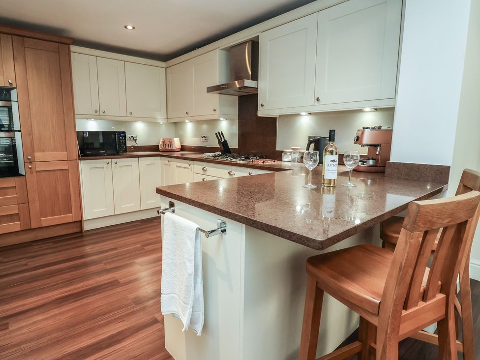 A kitchen with countertops, bar stools and kitchen appliances at 4 Green Farm Cottage in Saughall