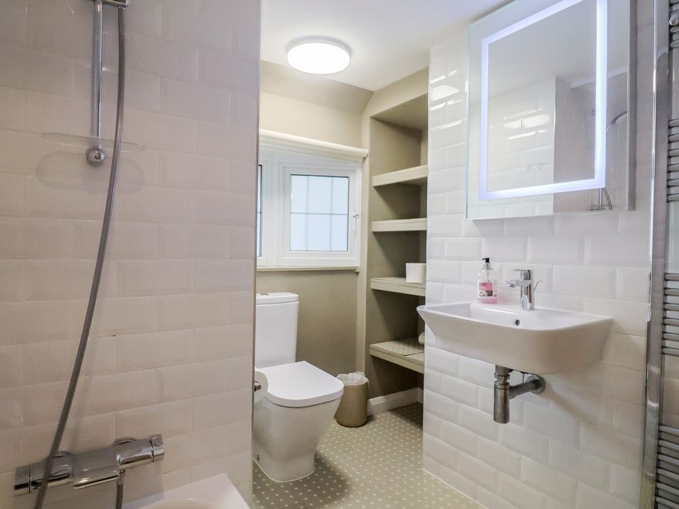 A bathroom with a shower, toilet, sink, and shelves at Maries in Lyme Regis
