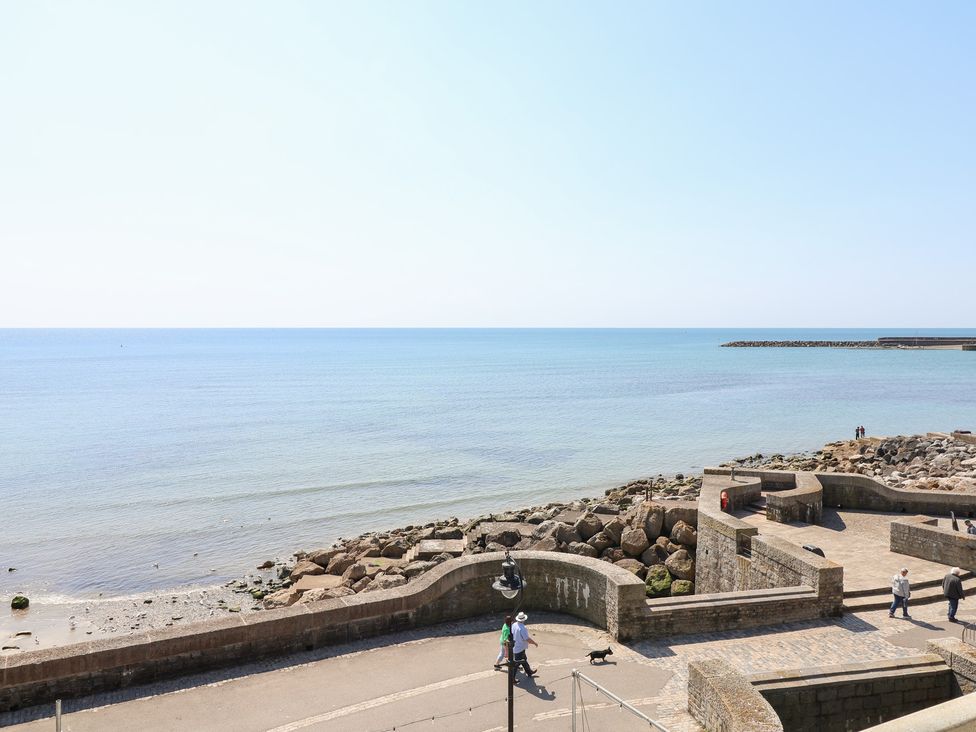 A seaside view with a promenade and people walking at Watersmeet Lyme Regis