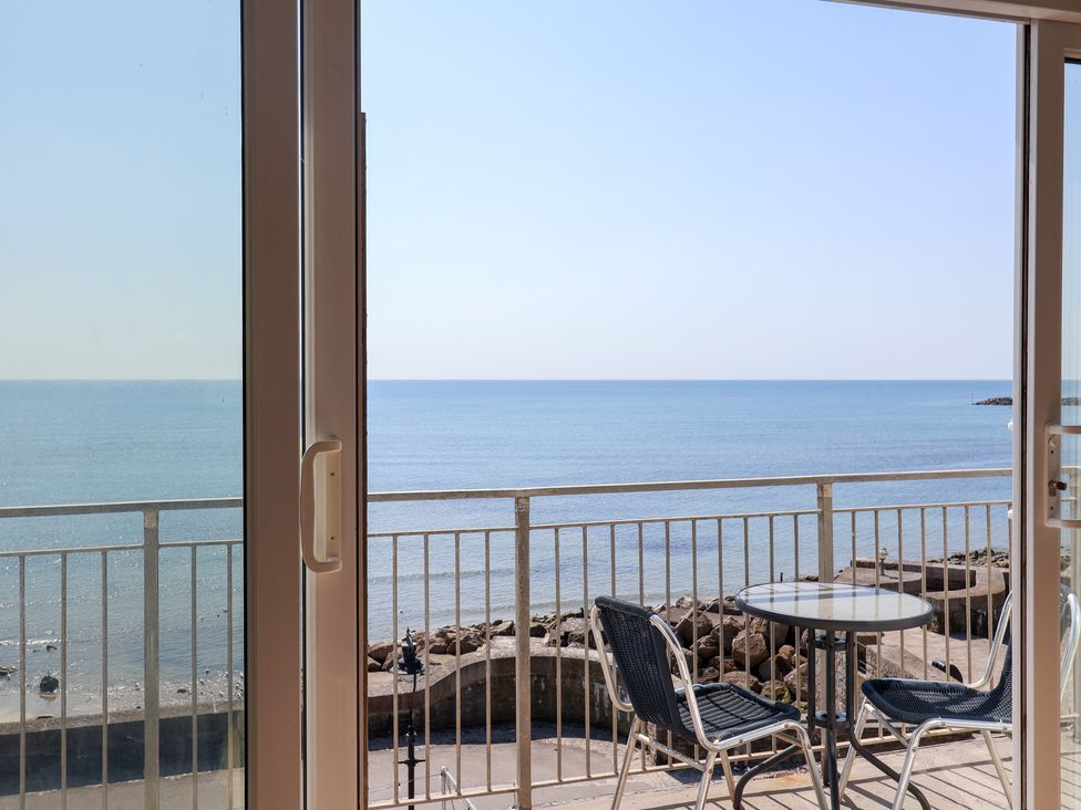 A balcony with a table and chairs overlooking the ocean at Watersmeet in Lyme Regis