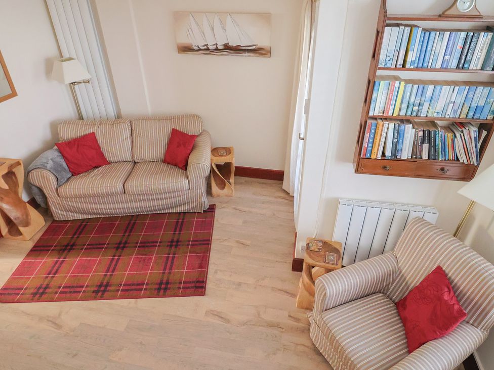 A living room with a sofa, armchair, bookshelf, and rug at 3 Dolphin Cottages in Lyme Regis